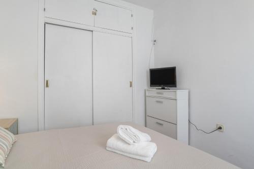 a white bedroom with a bed and a tv at Apartamento Playa Regla in Chipiona