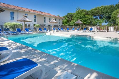 une grande piscine avec des chaises et des parasols bleus dans l'établissement Résidence Odalys Le Petit Pont, à Hourtin