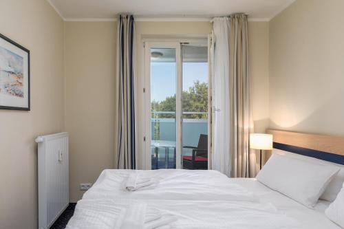 a bedroom with a white bed and a balcony at Seestern - Charmante 2-Zimmer-Wohnung mit Balkon in Zingst