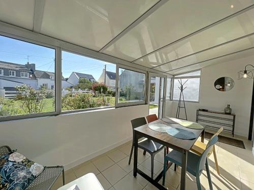 une salle à manger avec une table, des chaises et des fenêtres dans l'établissement Maison rénovée bord de mer avec véranda, jardin, 4 couchages, proche plages et commerces - FR-1-349-200, à Riantec