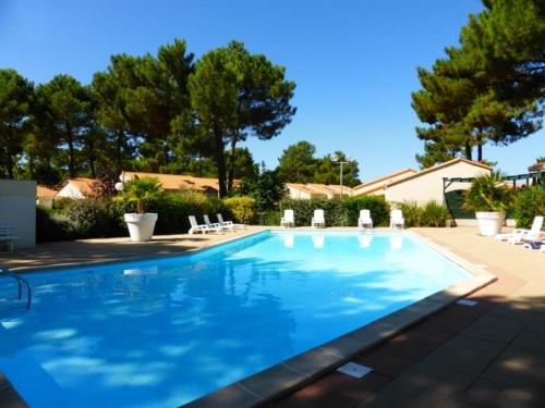 une grande piscine avec des chaises et des arbres dans l'établissement Location Vacances La Palmyre - Maison 4/5 pers. avec Piscine, Proche Plages & Commerces. - FR-1-705-6, à La Palmyre