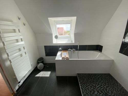 La salle de bains est pourvue d'une baignoire blanche et d'une fenêtre. dans l'établissement Gîte indépendant de charme avec piscine chauffée à Kervignac - 6 couchages, proche plages - FR-1-349-188, à Kervignac