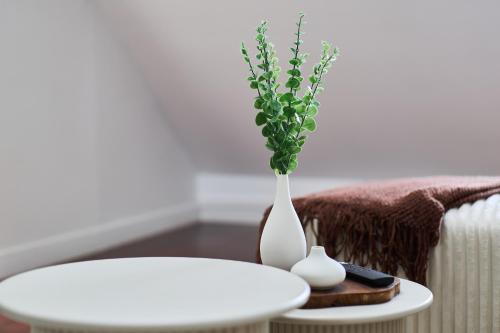 a white vase with a plant in it next to a table at Le Loft de la Porte de Mars - à 5 min de la gare in Reims