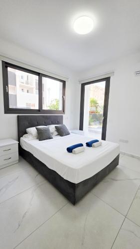 a large bed in a white room with windows at Poolside Lux Apartment in Larnaca