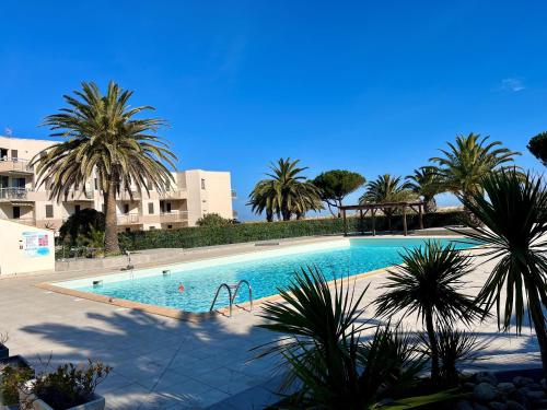 une grande piscine avec des palmiers en face d'un bâtiment dans l'établissement Appartement RDC avec Terrasse, Piscine & Accès Plage - St Cyprien, 4 Couchages - FR-1-753-27, à Saint-Cyprien