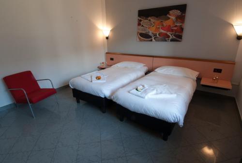a hotel room with two beds and a red chair at Hotel Bahnhof Haus in Chiasso