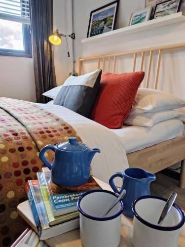 a bed with two blue tea pots on a table at Milking Shed Cottage in Narberth