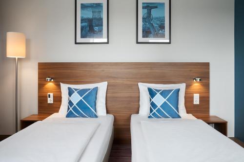two beds with blue and white pillows in a room at Four Points Flex by Sheraton Essen in Essen