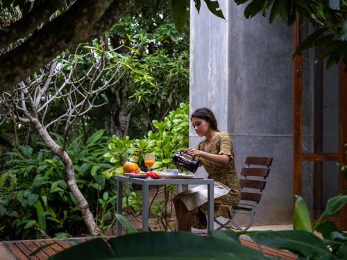 uma mulher sentada numa mesa num jardim em Kadju House em Tangalle
