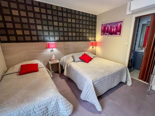 two beds in a hotel room with red pillows at La Bonne Auberge in Ségny