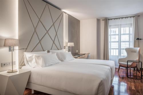 a white bedroom with a large white bed and a window at NH Collection Salamanca Palacio de Castellanos in Salamanca
