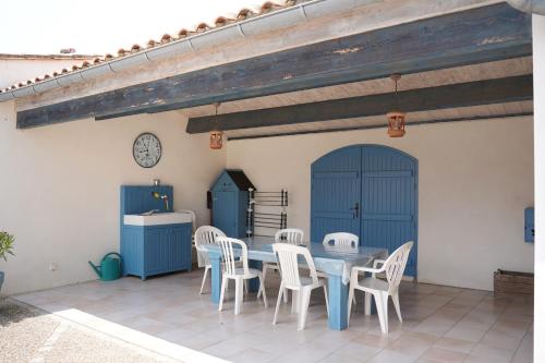une table et des chaises sur une terrasse avec portes bleues dans l'établissement Le Figuier, au Bois-Plage-en-Ré