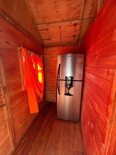a metal refrigerator in a room with wooden walls at Cabaña Selvática y Manantiales, San Miguel Guarne in Guarne