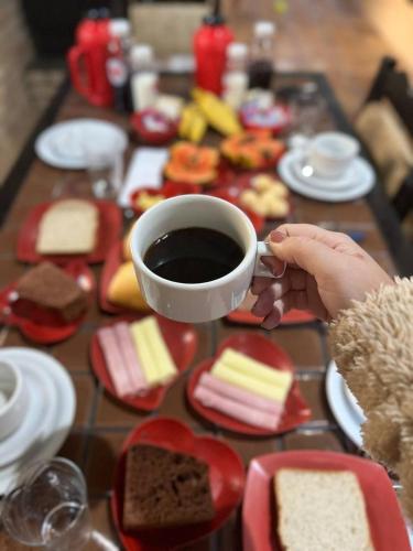 una persona che tiene in mano una tazza di caffè accanto a un tavolo di biscotti di Chalés do Holandês Eco Pousada a Bombinhas