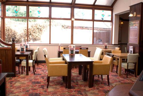 uma sala de jantar com mesas, cadeiras e janelas em George & Dragon em Coleshill