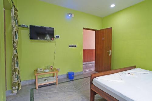 a green room with a bed and a tv on the wall at Whispering Woods Inn - Stay & Enjoy in Nature ! in Bolpur