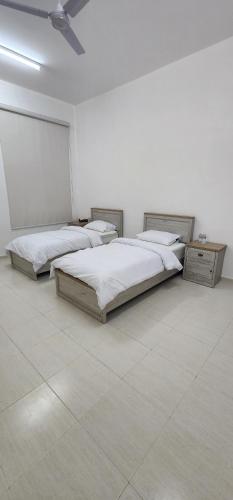 two beds in a room with white walls and tile floors at Hasik Beachfront Apartments in Ḩaḑbaram