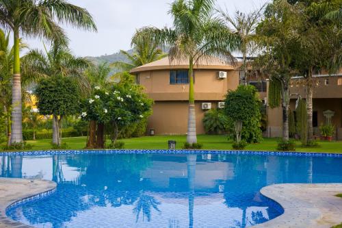 a swimming pool in front of a house with palm trees at Alaya Stays Jeevantara by ELIVAAS in Udaipur