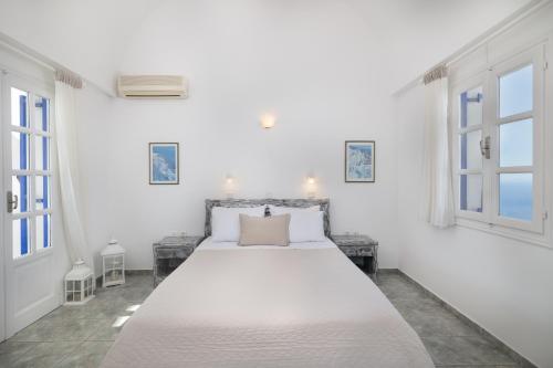 a white bedroom with a large bed and windows at Villa Happening in Imerovigli