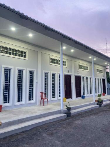 a white house with a red chair in front of it at Phnom Sampov Homestay ផ្ទះលំហែភ្នំសំពៅ in Phumĭ Kdaông Khang Tbong