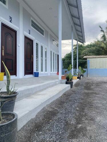 a white building with two brown doors and potted plants at Phnom Sampov Homestay ផ្ទះលំហែភ្នំសំពៅ in Phumĭ Kdaông Khang Tbong
