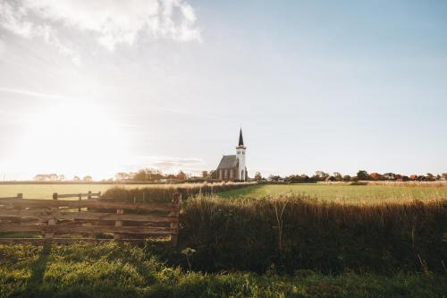 a church in the middle of a field with a fence at Boutique Hotel Texel in De Cocksdorp