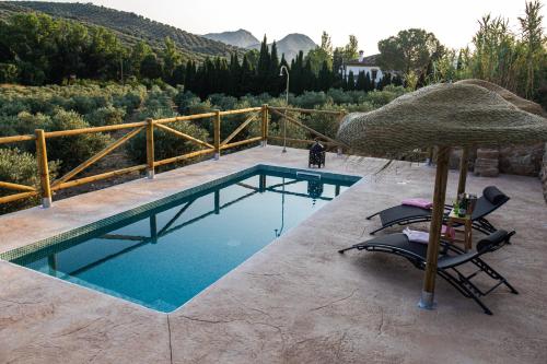 una piscina con dos sillas y una sombrilla en LA CASA DE LA HUERTA Stylish family cottage in Malaga countryside, en Málaga