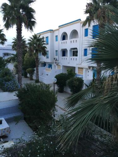 a large white building with palm trees and bushes at Appartement 3 chambres bords de mer Hammamet in Nabeul