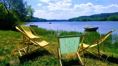 two chairs and a boat on the shore of a lake at Domek Wojtuś,wilcza chatka na Kaszubach koło Golubia,z balia i sauna,2 osobne sypialnie in Sikorzyno