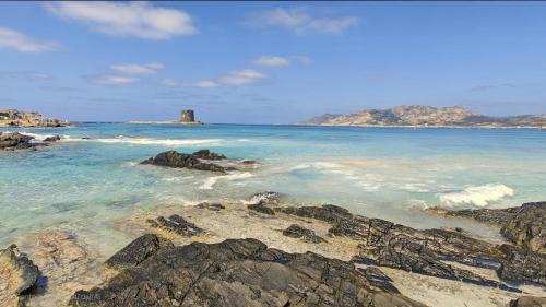 a beach with rocks and a lighthouse in the water at Villa Blu splendida villa con piscina - Stintino Sardegna in Cuile Pazzoni