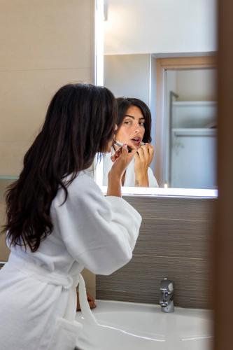 a woman brushing her teeth in front of a bathroom mirror at Hotel Villa Paola in Rimini