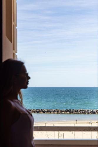 a woman looking out a window at the ocean at Hotel Villa Paola in Rimini