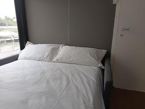 a bed with white sheets and pillows next to a window at DIAMOND Bigigio House Boat in Lisanza