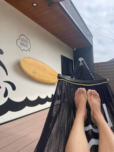 a person laying in a hammock with their feet on a surfboard at Glam Pool Terrace Shizunami in Makinohara