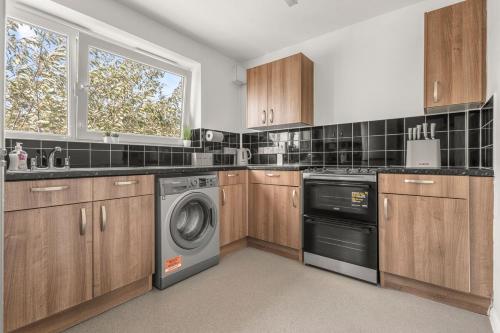 バーキングにあるBright & Modern London Apartmentのキッチン(木製キャビネット、洗濯機、乾燥機付)