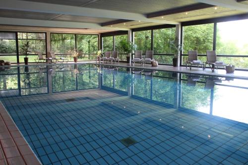 a large swimming pool with chairs and windows at Hotel Landhaus Höpen in Schneverdingen