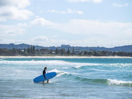 a man standing in the ocean holding a surfboard at YHA Cape Byron, Byron Bay in Byron Bay