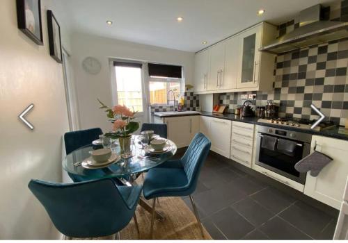 a kitchen with a glass table and blue chairs at Flamingo Short Lets Greenleys in Wolverton