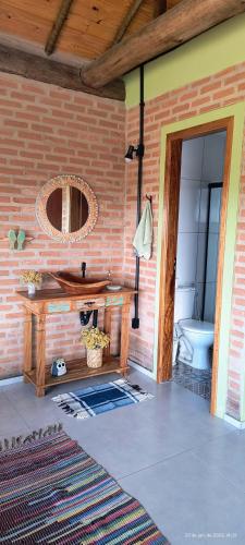 a room with a brick wall with a table and a toilet at Chalé estrela do cruzeiro in São Thomé das Letras