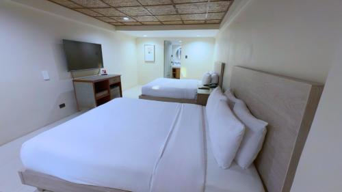 a bedroom with two white beds and a television at Whiterock Beach Hotel and Waterpark in Subic