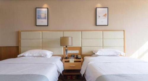 a hotel room with two beds and a lamp on a table at The Prosperous City Hotel Weifang in Weifang