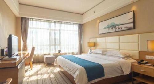 a bedroom with a bed and a desk and a television at The Prosperous City Hotel Weifang in Weifang