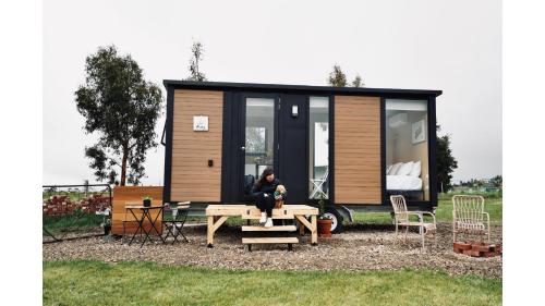 a woman sitting at a picnic table in front of a tiny house at Maluridae Creek Views by Tiny Away in Lawrence