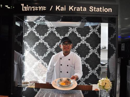 a chef holding a plate of food in a kitchen at Tanzeno Hotel in Nong Khai