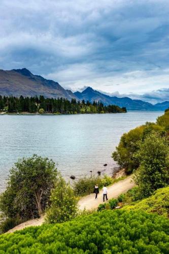 two people walking on a dirt path next to a lake at Oaks Queenstown Club Suites in Queenstown