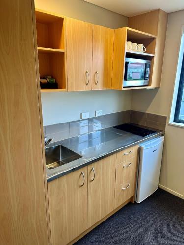 a kitchen with wooden cabinets and a sink and a dishwasher at Pokeno Motel in Pokeno