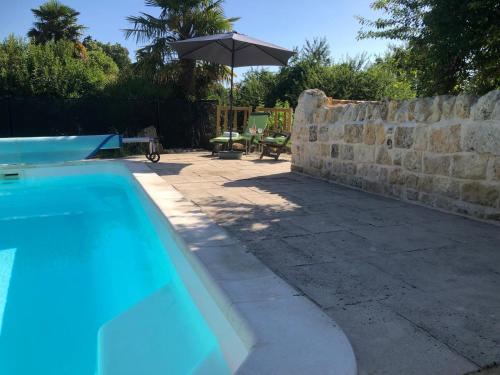- une piscine avec un parasol à côté d'un mur en pierre dans l'établissement Le Jardin des Bosquets, à Auzay