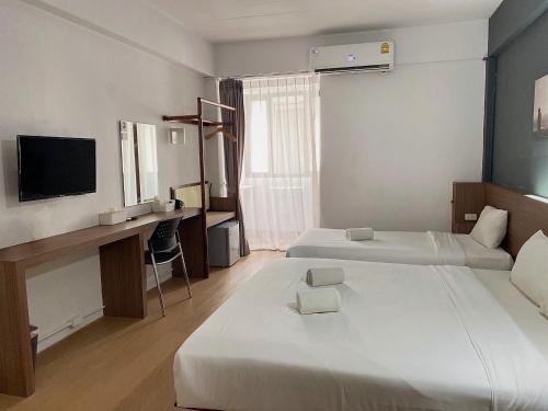 a room with two beds and a desk and a television at Shane Hotel in Chiang Mai