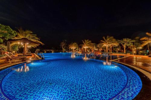 a large blue swimming pool with palm trees at night at HON BA LAGI BEACH RESORT in La Gi