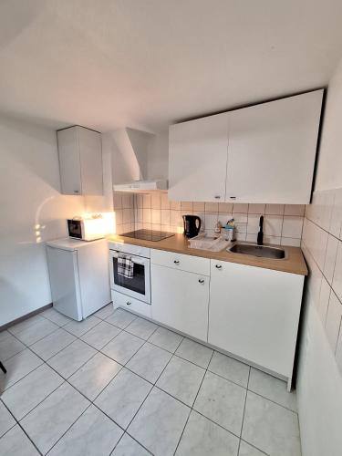 a kitchen with white cabinets and a sink and a refrigerator at Helmstedt City Apartment in Helmstedt